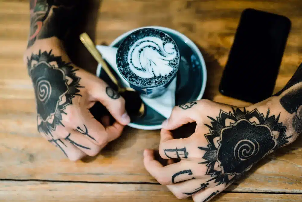 manos tatuadas manos sosteniendo un vaso con cafe